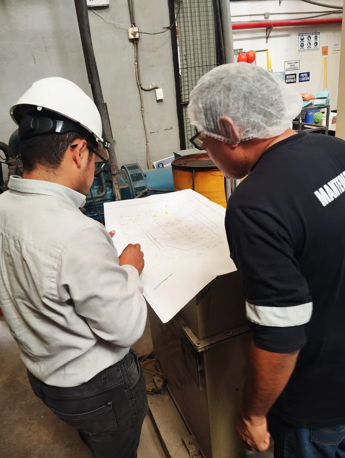 Dos hombres con cascos miran un trozo de papel.