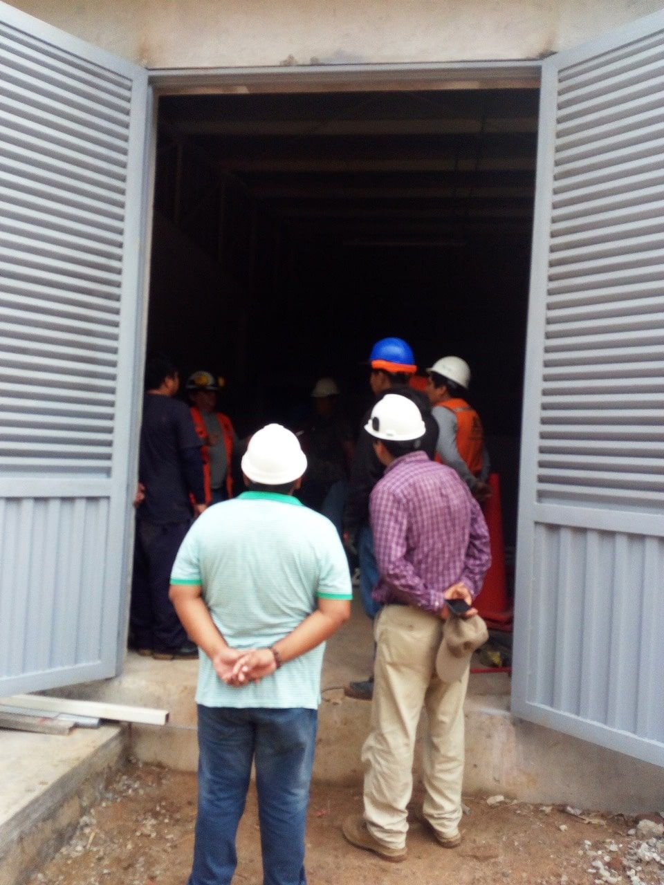 Un grupo de hombres con cascos de seguridad están parados afuera de un edificio.