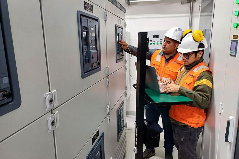 Dos hombres están trabajando en una computadora en una sala eléctrica.
