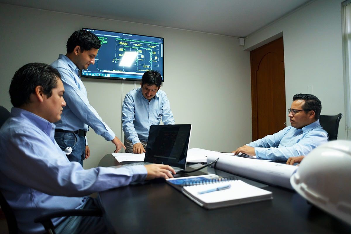 Un grupo de hombres están sentados alrededor de una mesa mirando una computadora portátil.