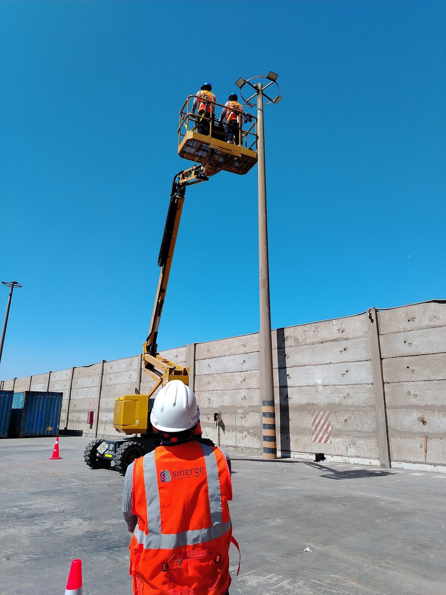 Un hombre con un chaleco naranja se encuentra frente a una grúa.