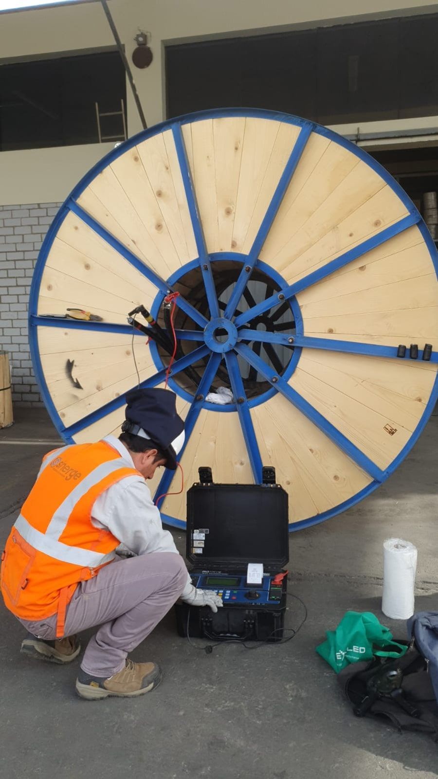 Un hombre está arrodillado frente a un gran carrete de madera.