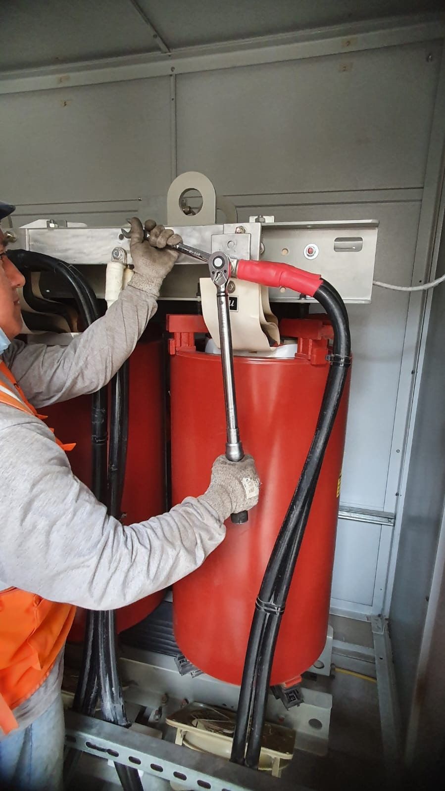 Un hombre está trabajando en un transformador rojo con una llave inglesa.