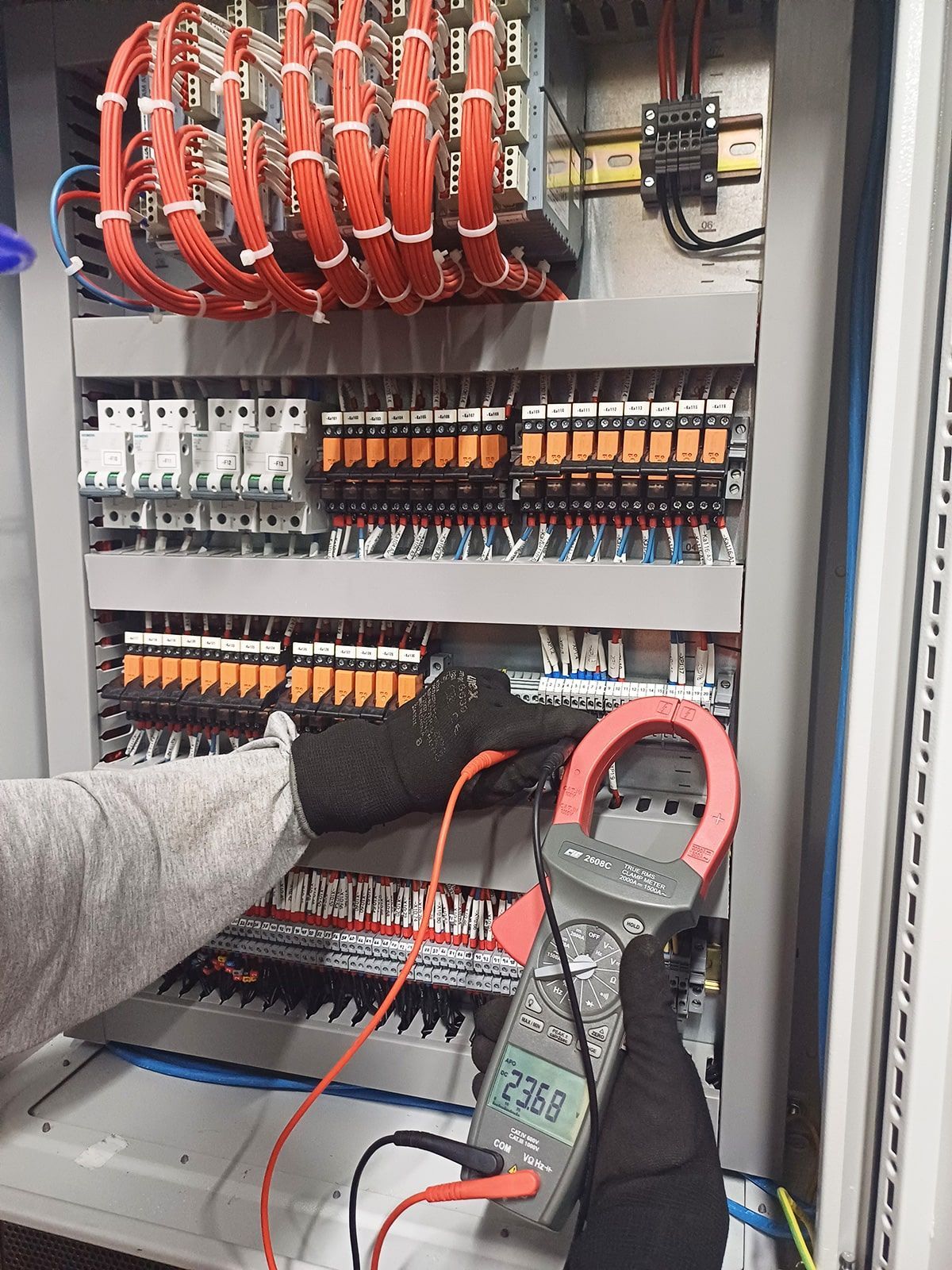 Una persona está usando una pinza amperimétrica para comprobar un panel eléctrico.
