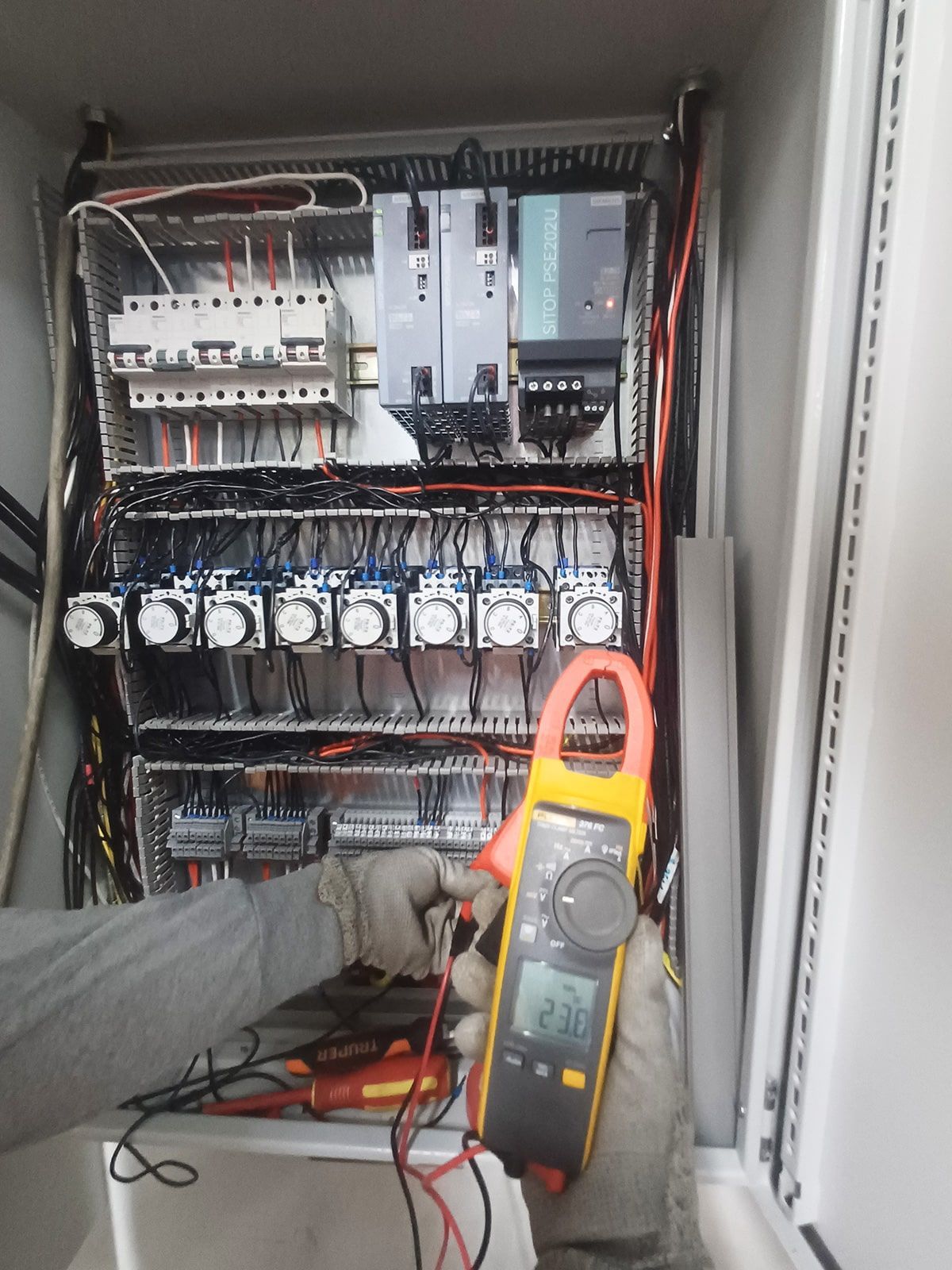 Una persona sostiene una pinza amperimétrica delante de una caja eléctrica.
