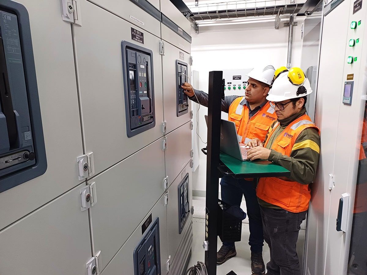 Dos hombres están trabajando en una computadora en una sala eléctrica.