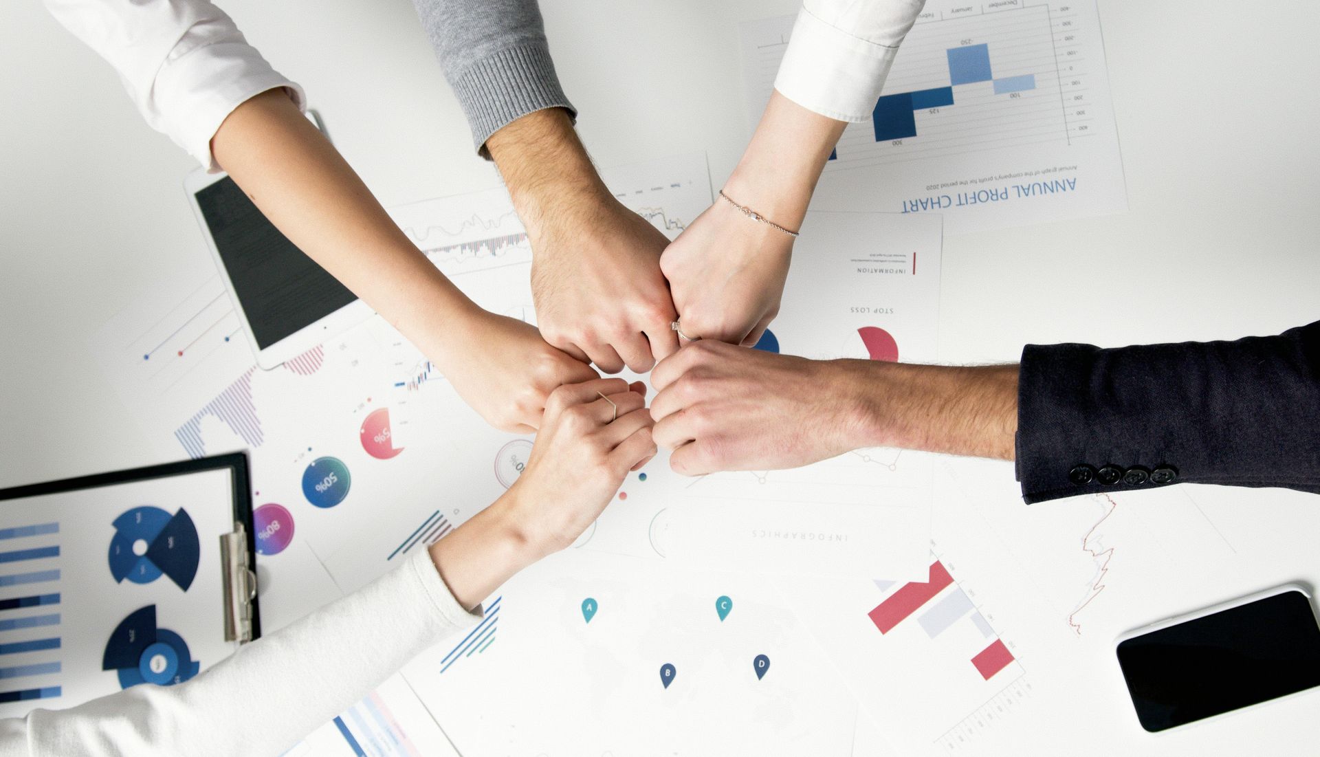 Team of hands clasped together over a table with charts and a phone, symbolizing teamwork.