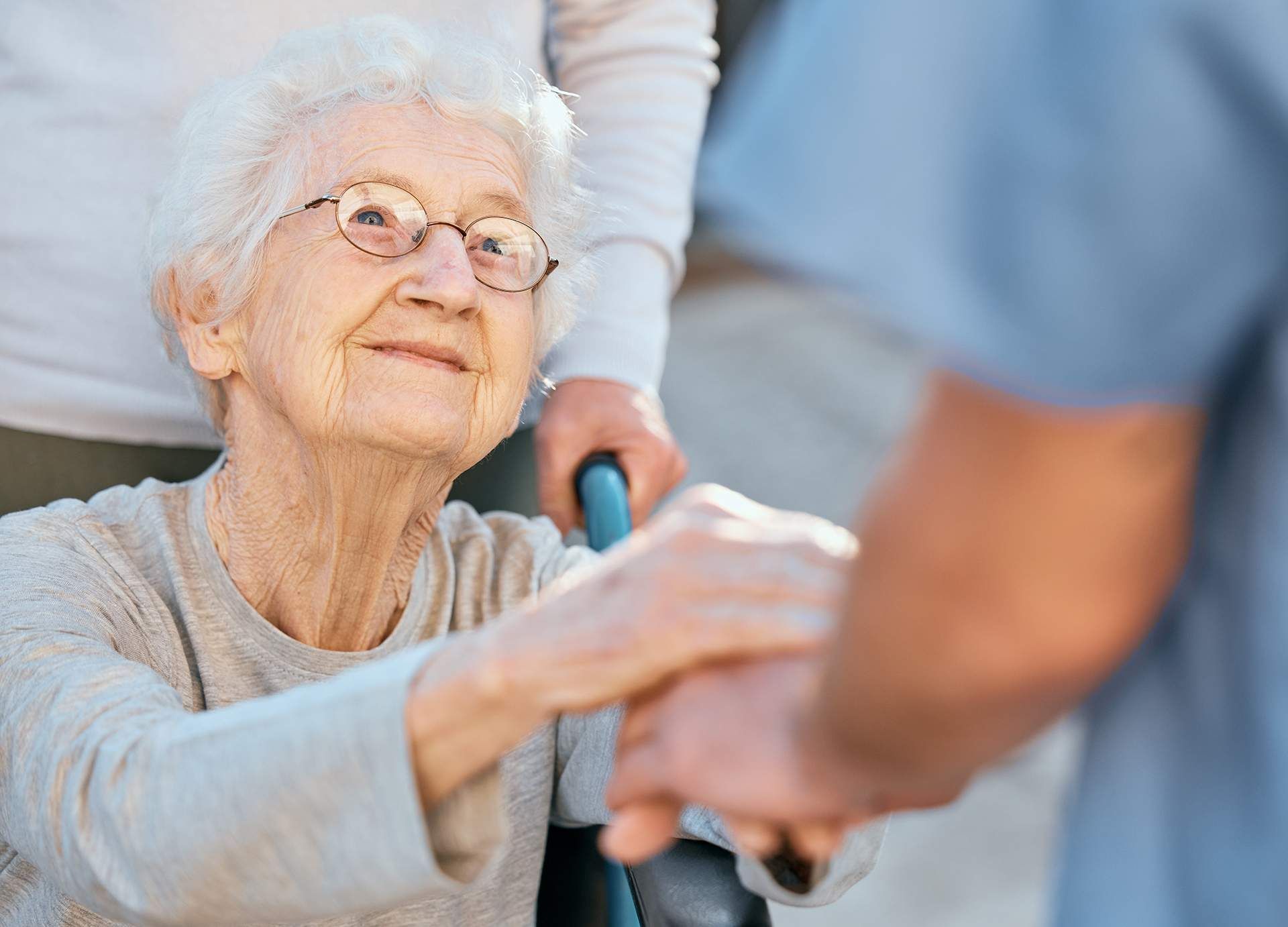 Elderly woman smiling while holding hands with a caregiver in a bright indoor setting