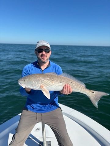 Man on boat holding large redfish. Blue water and sky.