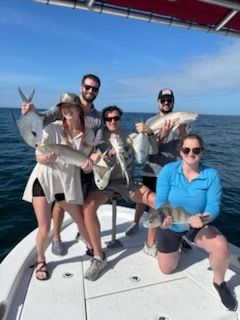 Group of people on a boat, holding up fish they caught. Blue water, sunny sky.
