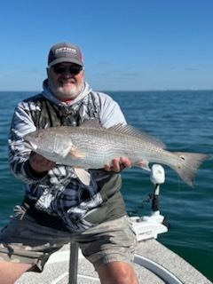 Man holding a large redfish on a boat, blue water and sky in background.