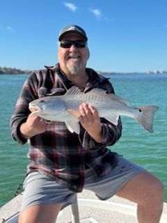 Man in sunglasses holds a fish on a boat; turquoise water, blue sky.