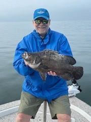 Man in blue jacket and hat holding a large black fish on a boat.