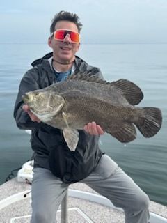 Man in sunglasses holding a large dark fish on a boat.