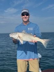 Man holding a redfish on a boat, blue water, sunny day.