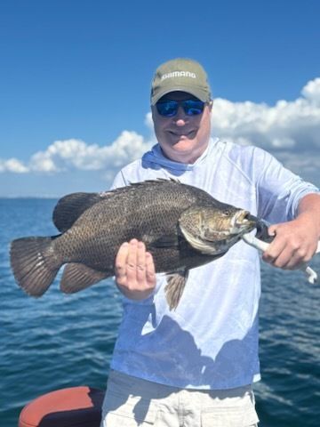 Man holding a large black fish caught on a boat in sunny weather.