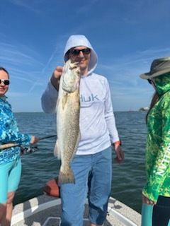 Man on boat holding up a fish, two others nearby. Ocean, sunny sky.