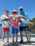 Three people holding up fish on a boat. Sunny day. Two children and an adult smiling.