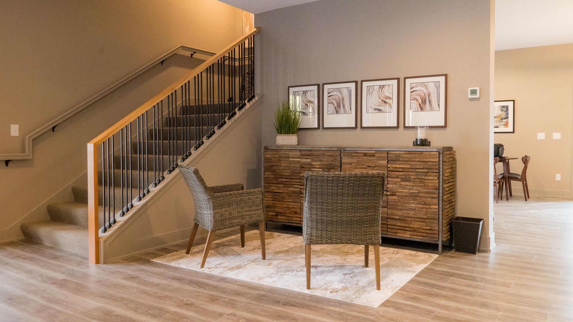 A living room with stairs , chairs , a dresser and a rug.