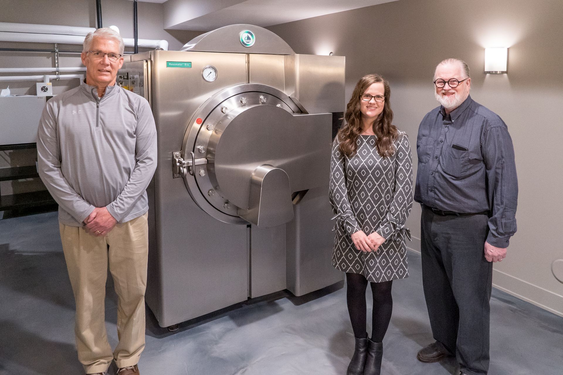 Three people are standing in front of a large stainless steel machine.