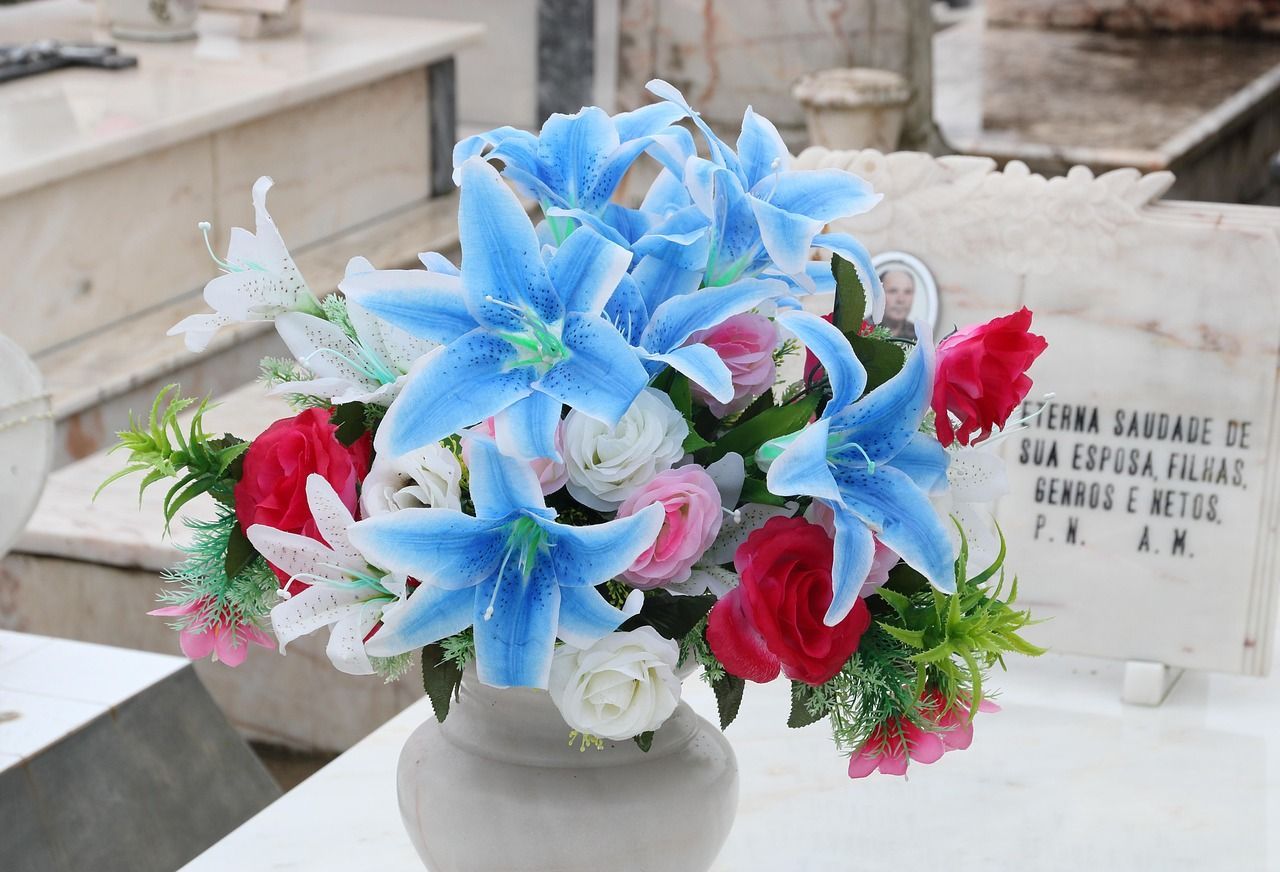 Vase of blue lilies, red roses, and white flowers placed on a cemetery headstone