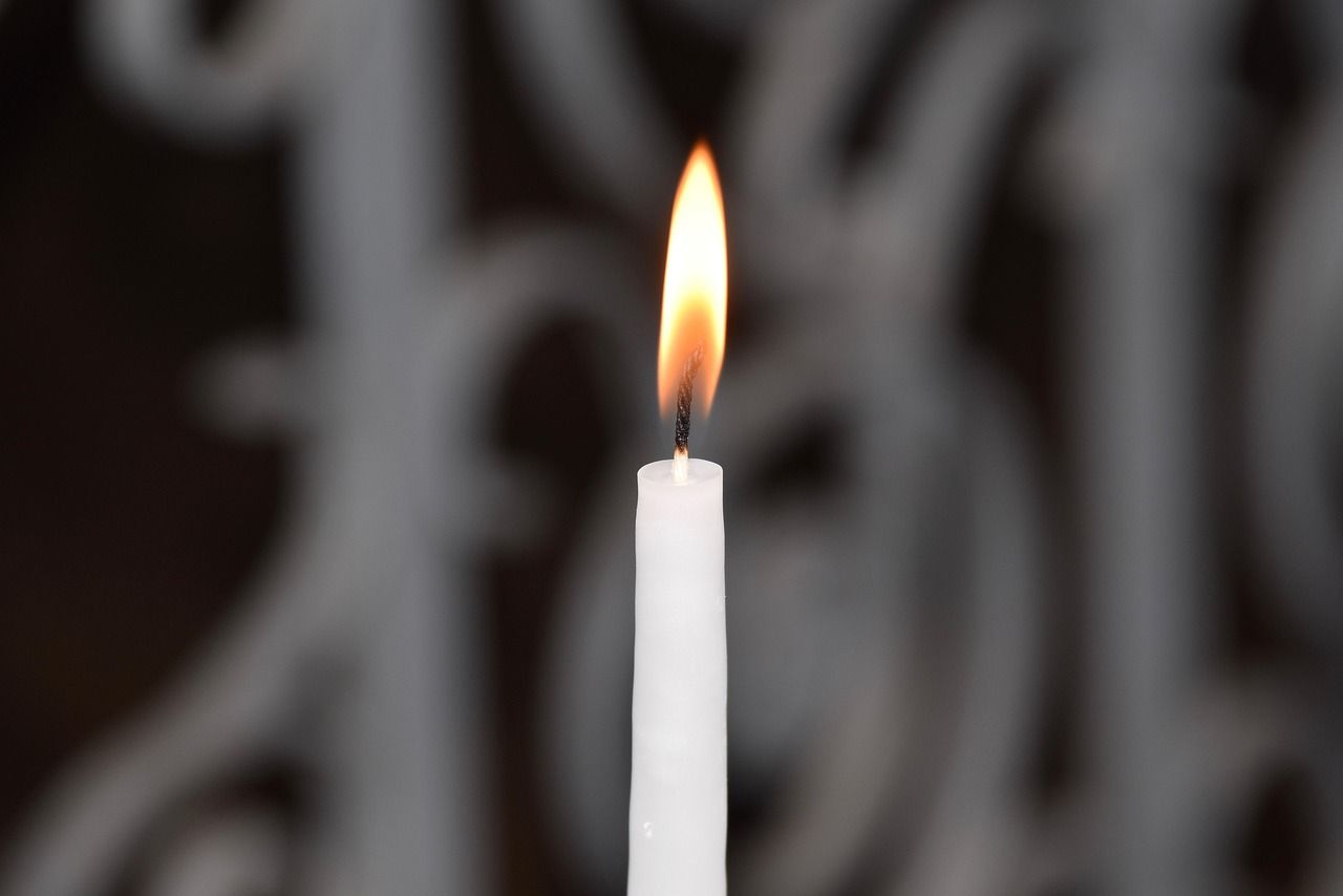 Single white memorial candle burning with a soft flame against a dark background