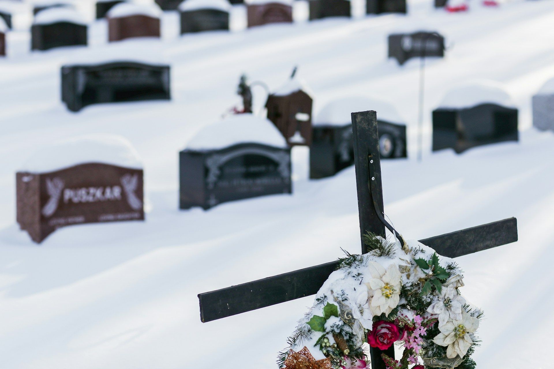 Cross with a wreath resting on top, standing in snowy surroundings symbolizing honor and remembrance.