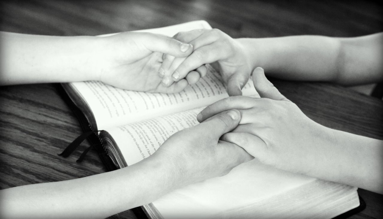 Family and friends holding hands in prayer with a Bible, reflecting faith and compassionate support from funeral homes Jordan, MN.
