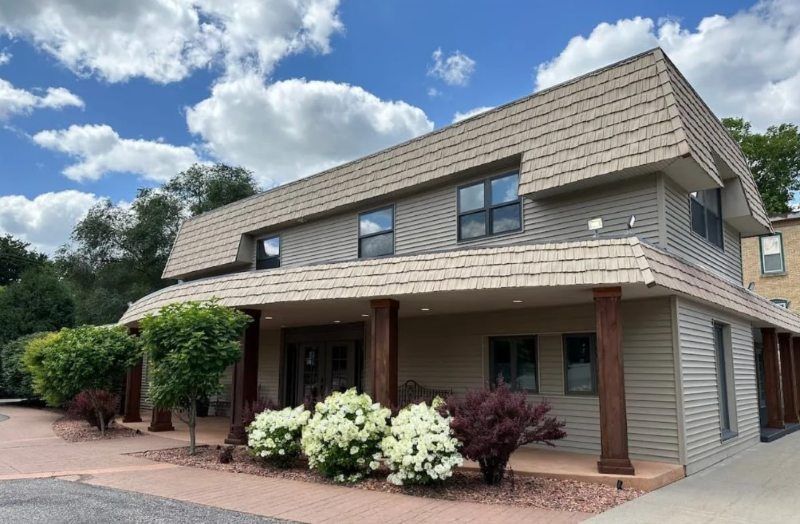 A modern two-story building with landscaped flowers and wood columns representing a Jordan, MN funeral home and cremations facility.