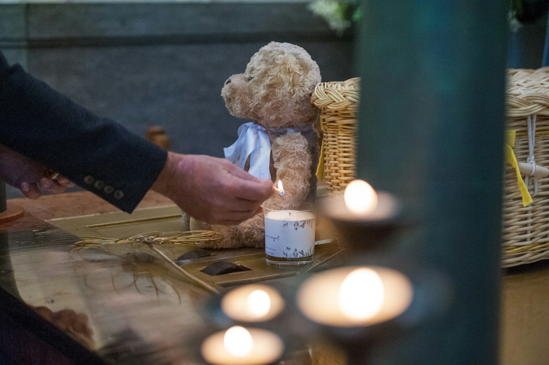 Person lighting a candle beside a teddy bear as a heartfelt memorial tribute. 