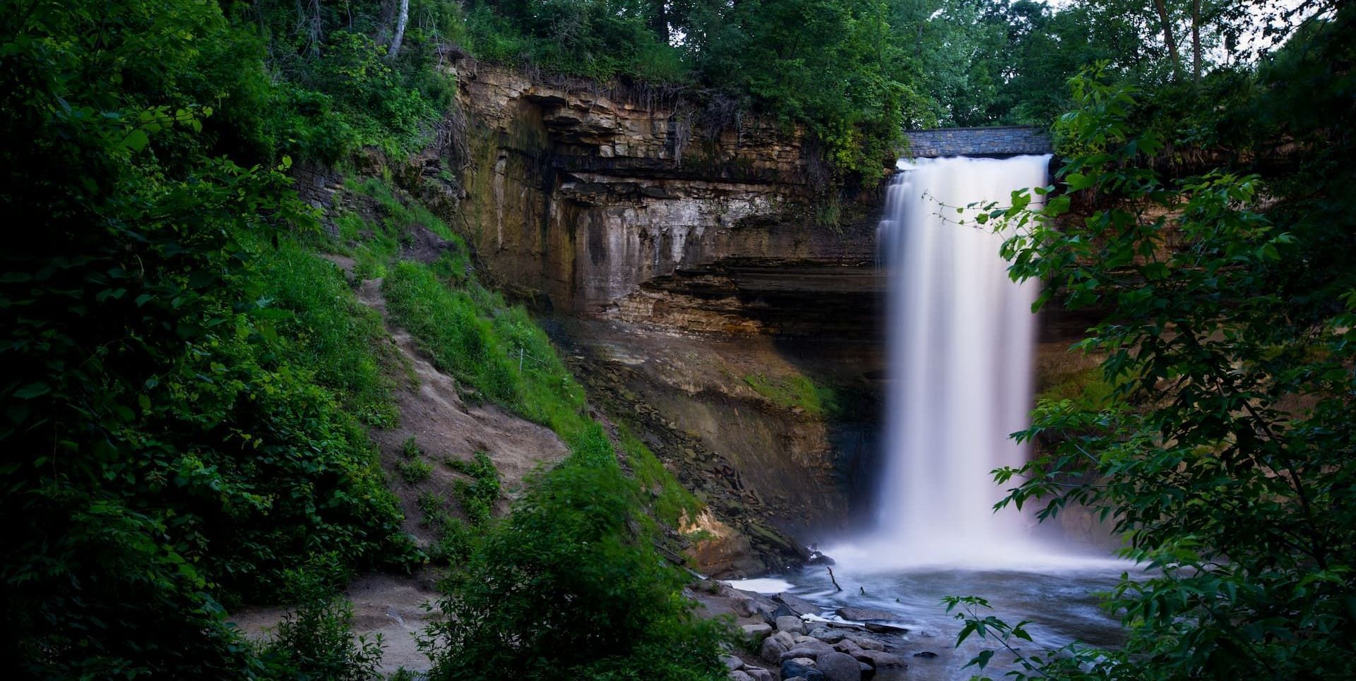 A waterfall is surrounded by trees and rocks in the middle of a forest.