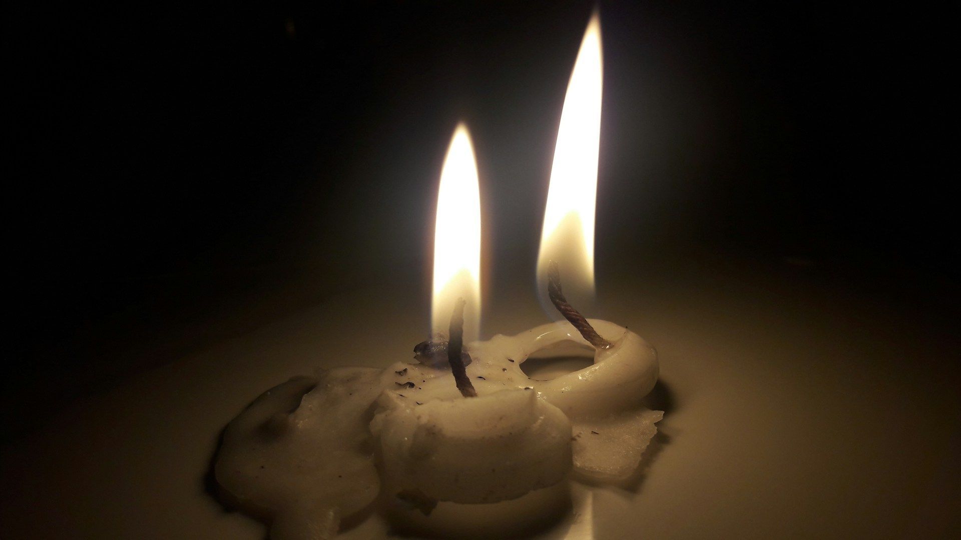 Single white candle on a plain white surface symbolizing peace, prayer, and solemn remembrance.