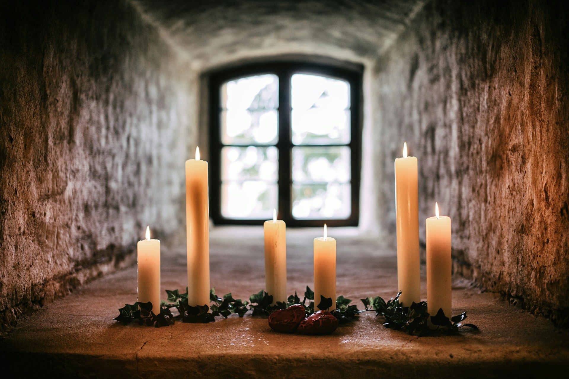Six white taper candles standing on gray concrete pavement, evoking serene reflection and solidarity.