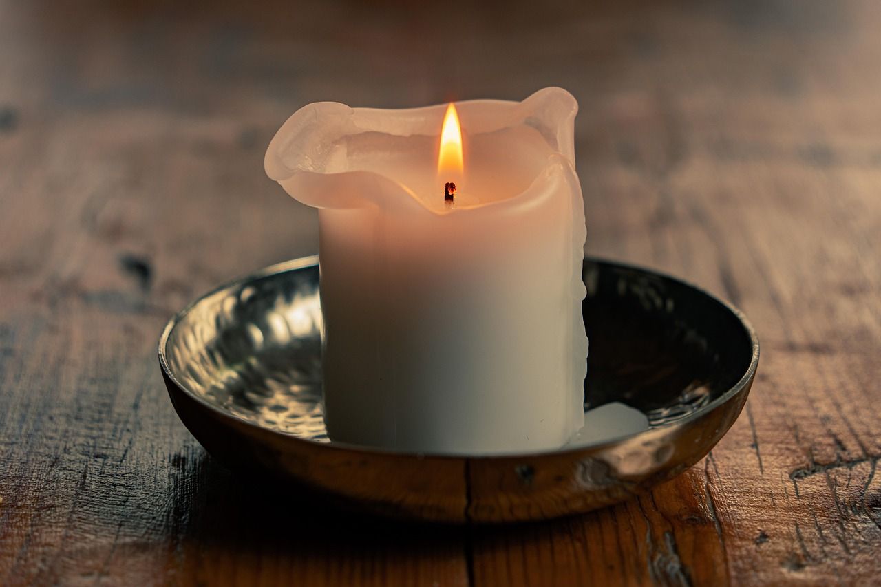 Single candle flame glowing softly in the dark, evoking warmth, solace, and peaceful reflection.