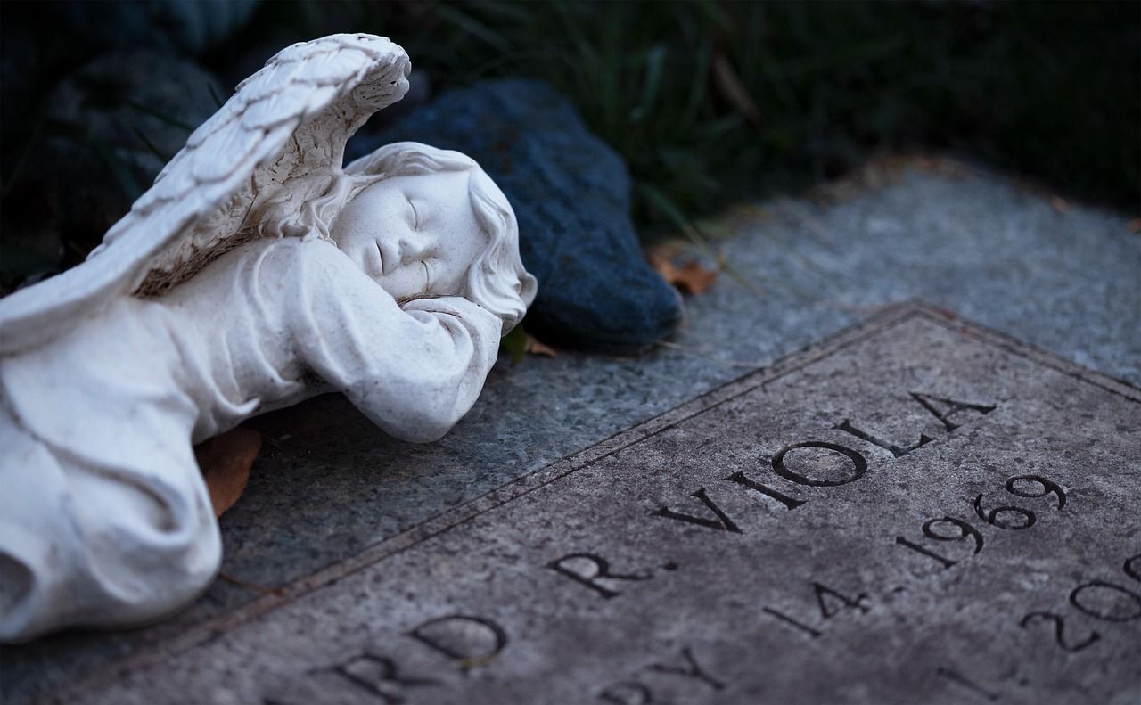 Stone angel statue standing beside a tombstone in a cemetery evoking reflection and memory.
