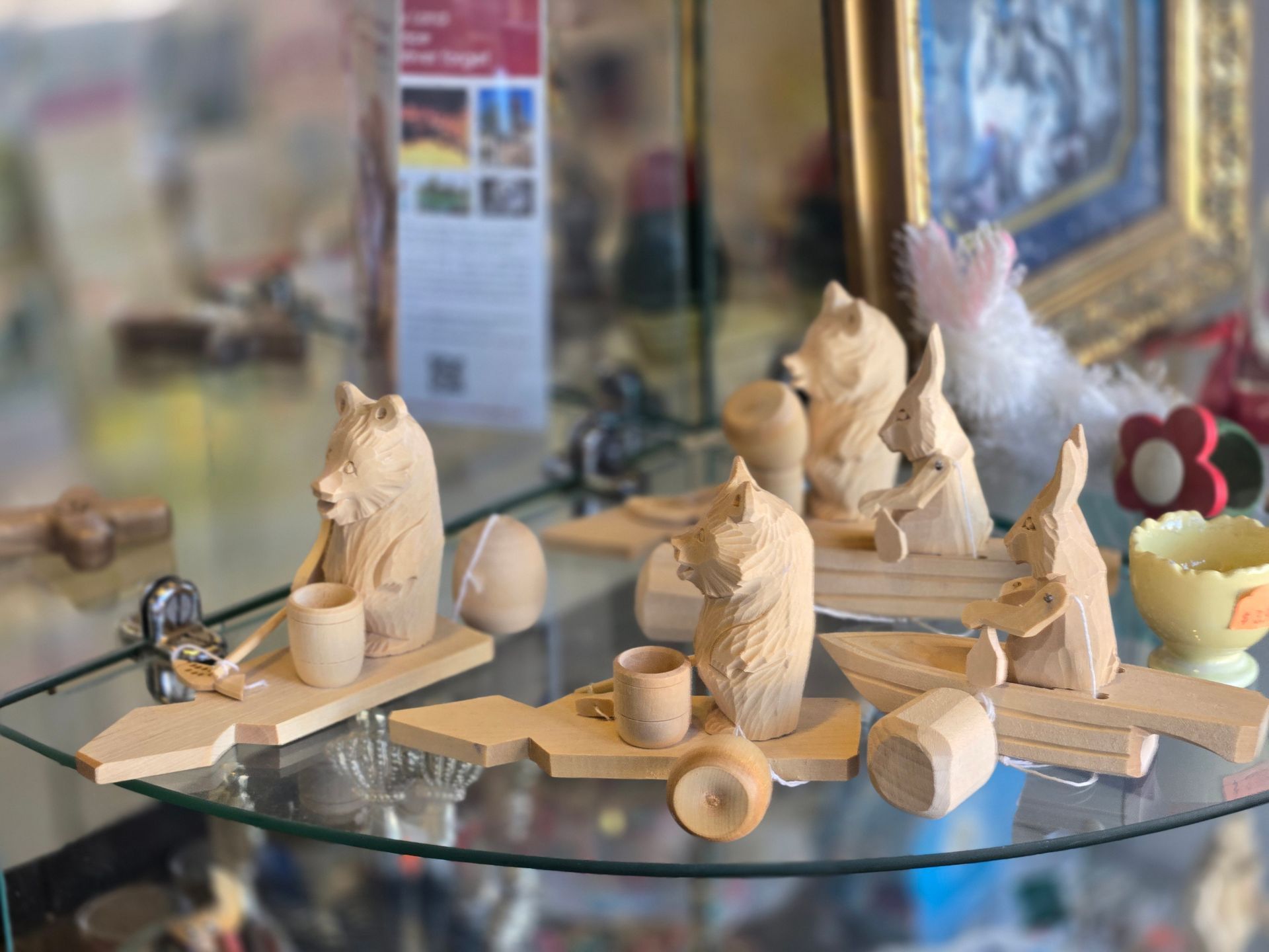 Wooden carved bear figurines seated at tables, some holding mugs. Glass display shelf, shop setting.