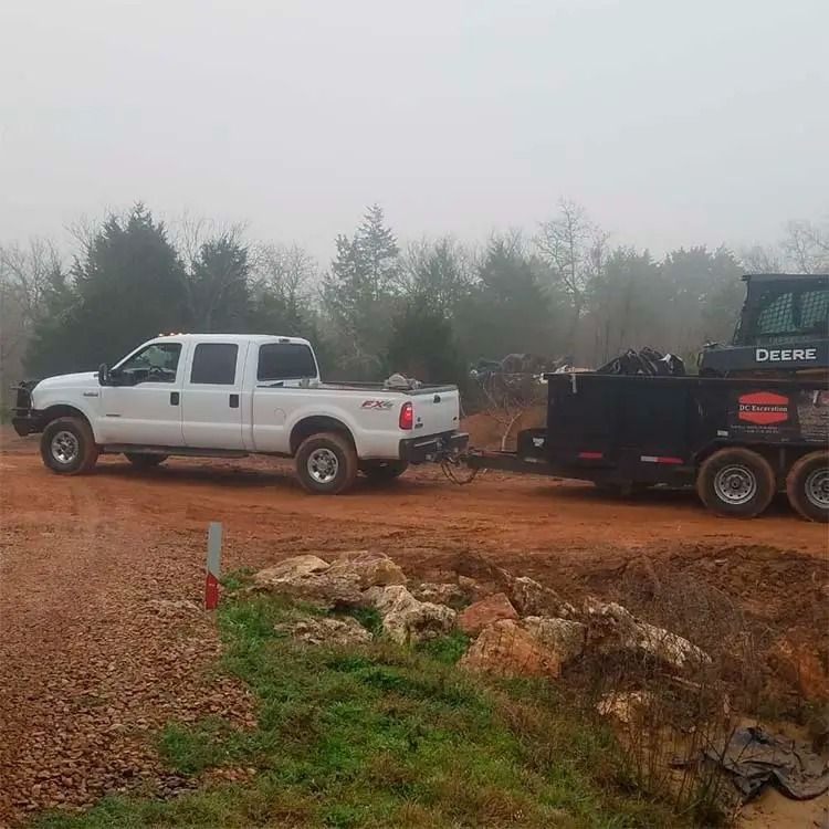 White pickup truck towing a black trailer on a muddy dirt road in foggy woods