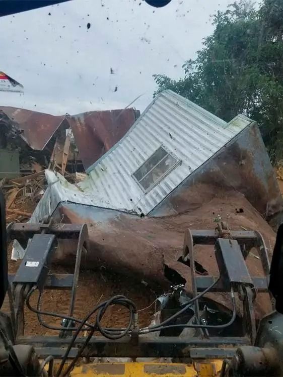 Collapsed house in storm damage, with a white roof and debris amid heavy rain.