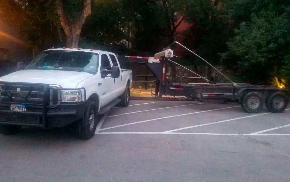White pickup truck towing a flatbed trailer in a parking lot at dusk