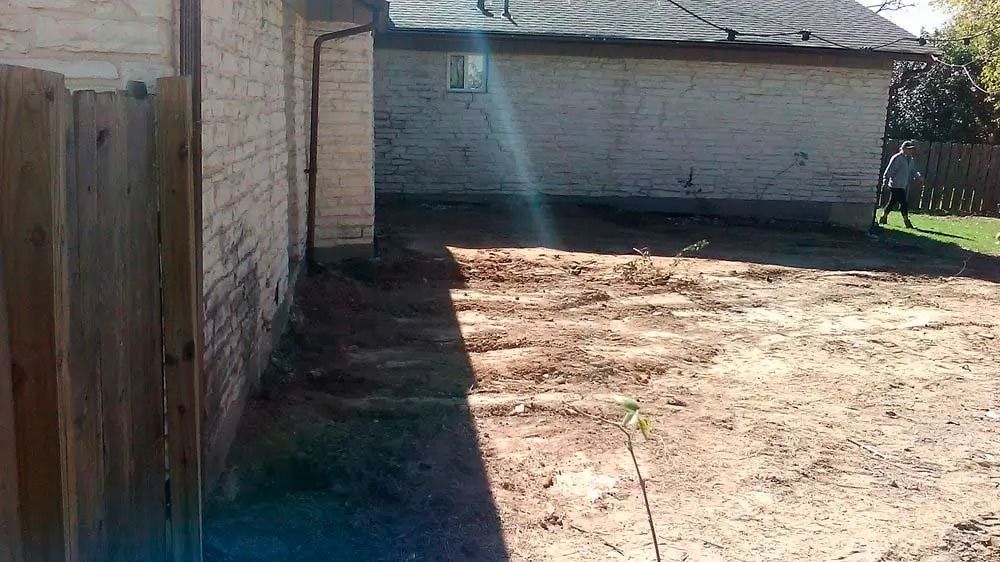 Backyard with a dirt lot, brick wall, wooden fence, and a garage in bright sunlight