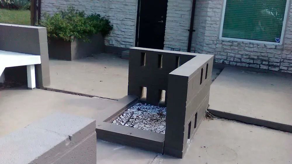 Outdoor patio with black metal fire pit filled with white stones beside benches and planters