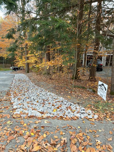 Gravel border along a driveway in a wooded area with fall foliage.