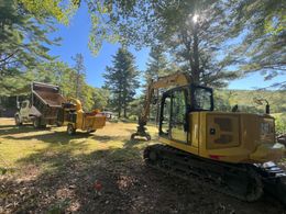 Yellow excavator and wood chipper on a grassy area under a sunny sky.