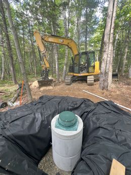 Excavator near a newly installed septic tank in a wooded area.