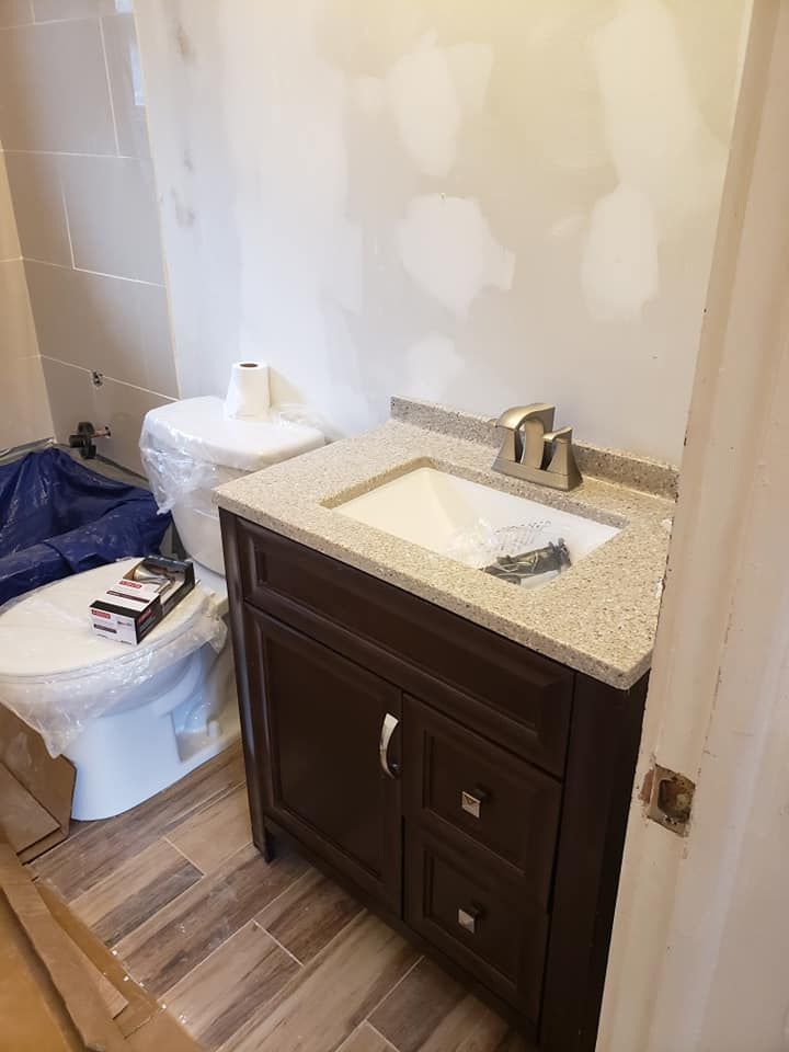 Bathroom renovation: Dark brown vanity with a light-colored countertop next to a white toilet. Unfinished wall.