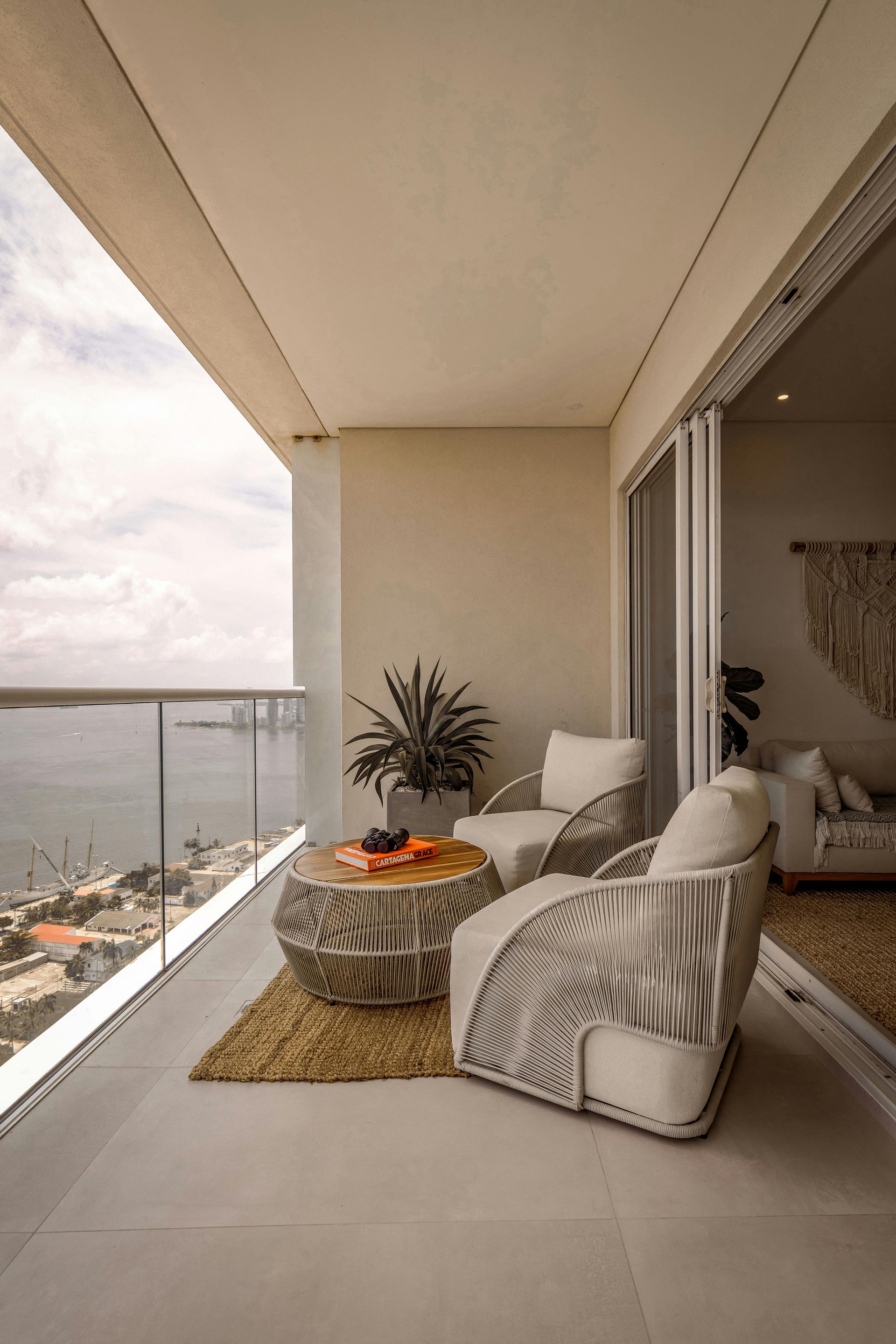 Balcony with two patterned chairs, table, and plant, overlooking water and city.