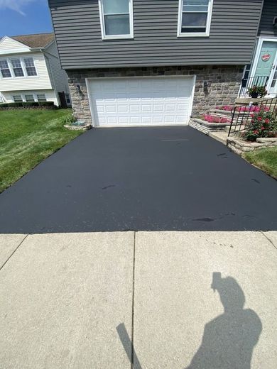 A black driveway with a white garage door is in front of a house.