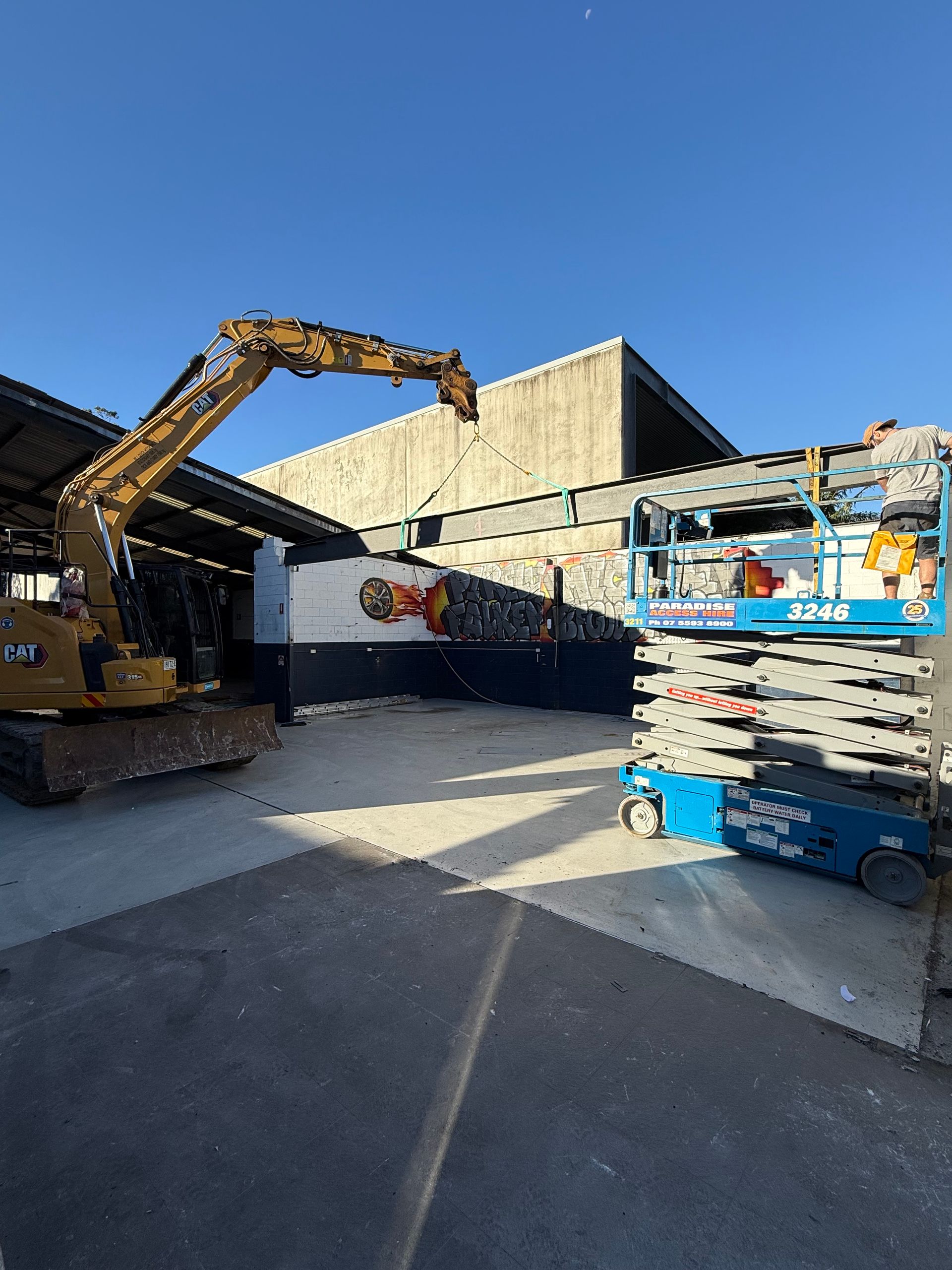 An excavator and a lift in a construction area, under a blue sky.