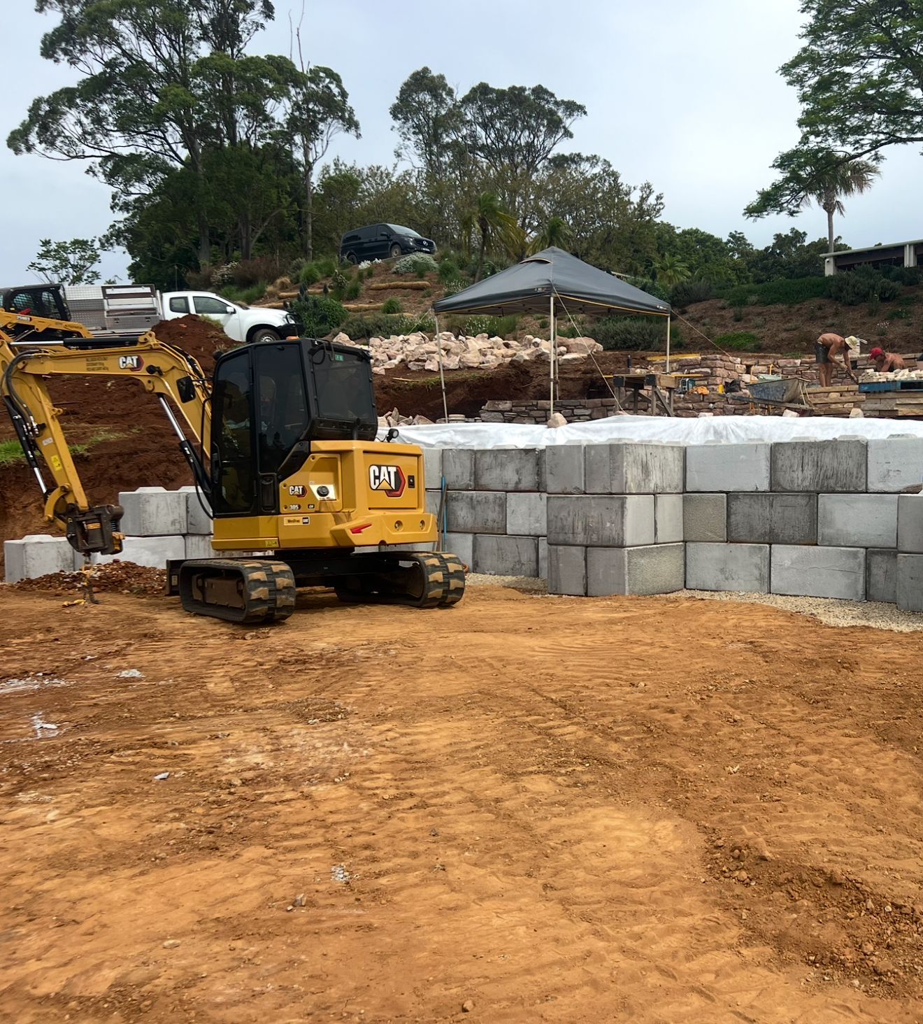 Yellow excavator building a retaining wall with concrete blocks on a construction site.