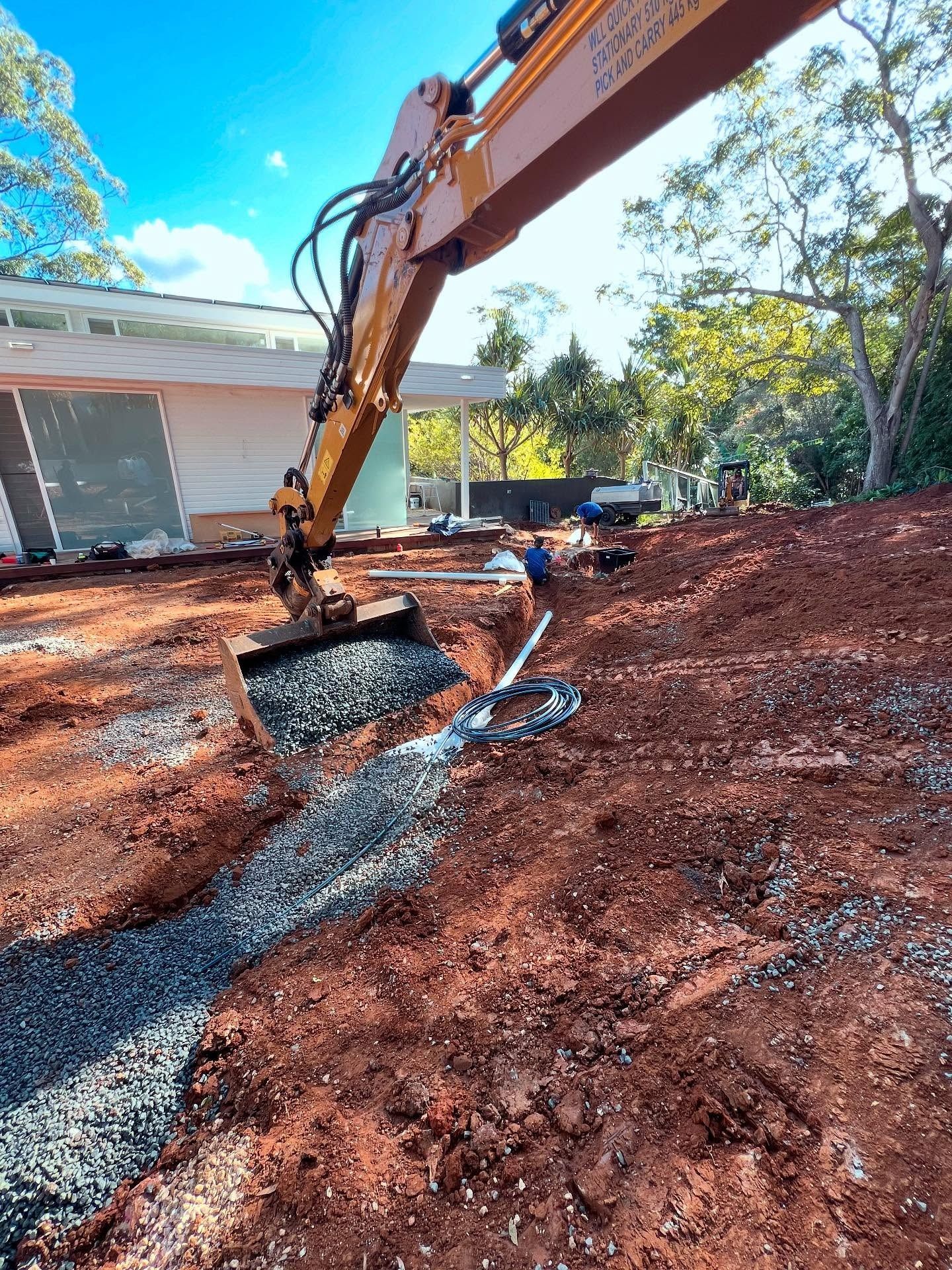 Excavator Pouring Gravel Into a Trench at A Construction Site  — Bigfoot Earthmoving In Byron Bay, NSW